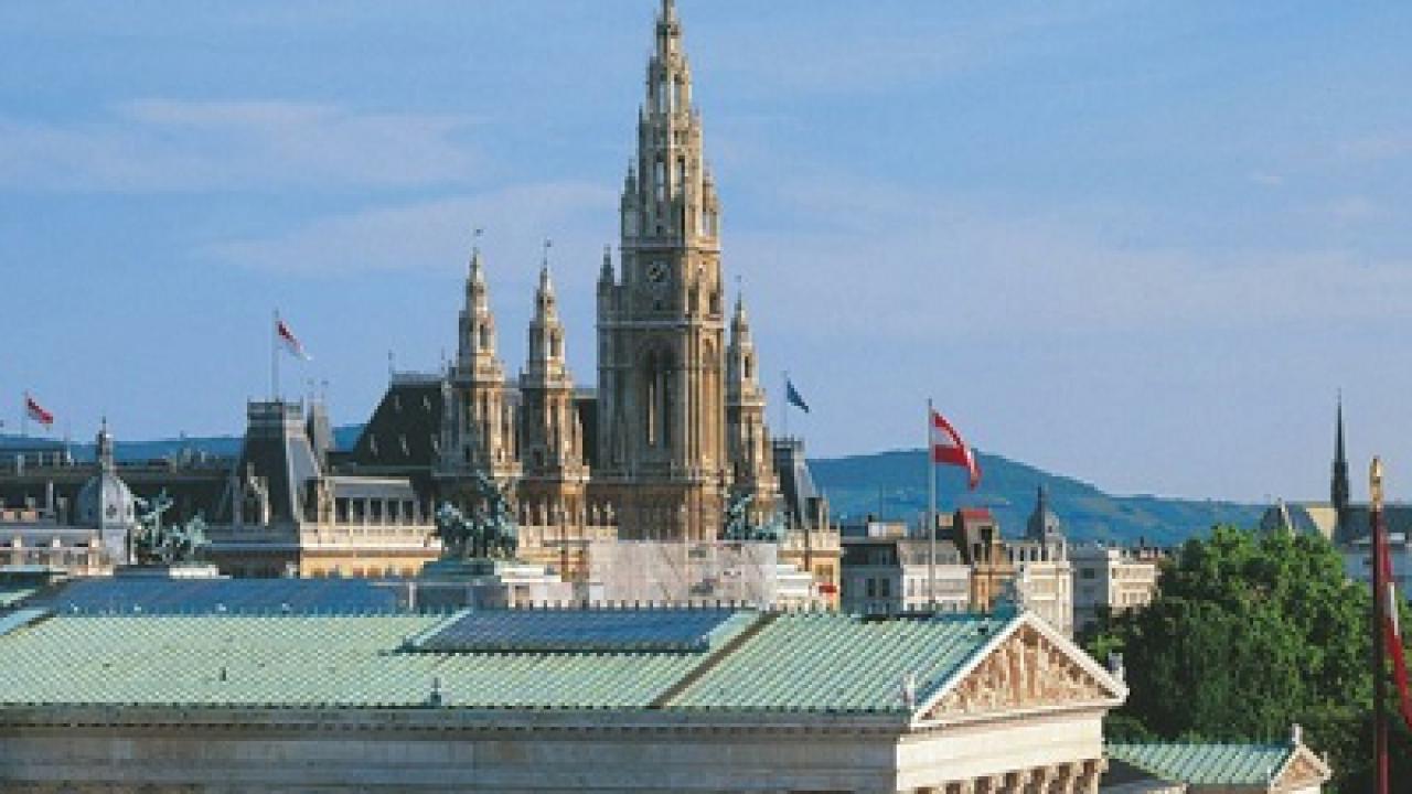 Panoramic city skyline with ornate Gothic spire, green rooftops under blue sky