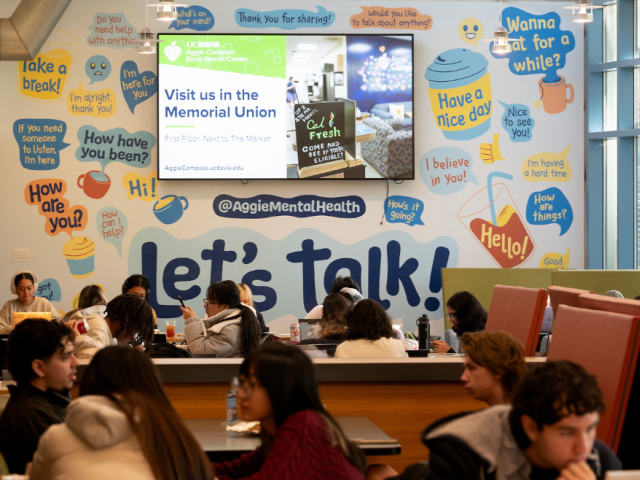 Campus dining area with students at booths under a colorful "let's talk!" mural