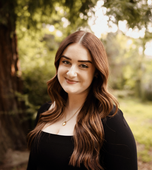 A photo of a woman with brown hair, a tree in the background.
