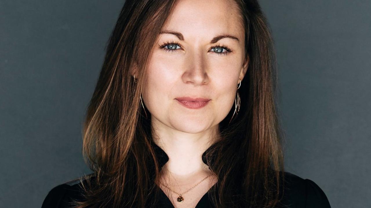 A headshot of a woman with brown hair against a grey background