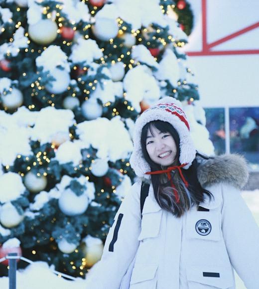 A person in a white jacket standing in front of a snow-covered Christmas tree