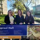 Three women standing behind a sign