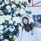 A person in a white jacket standing in front of a snow-covered Christmas tree