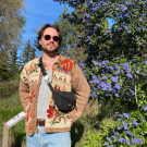 A man wearing a tan floral jacket stands in front of a tree